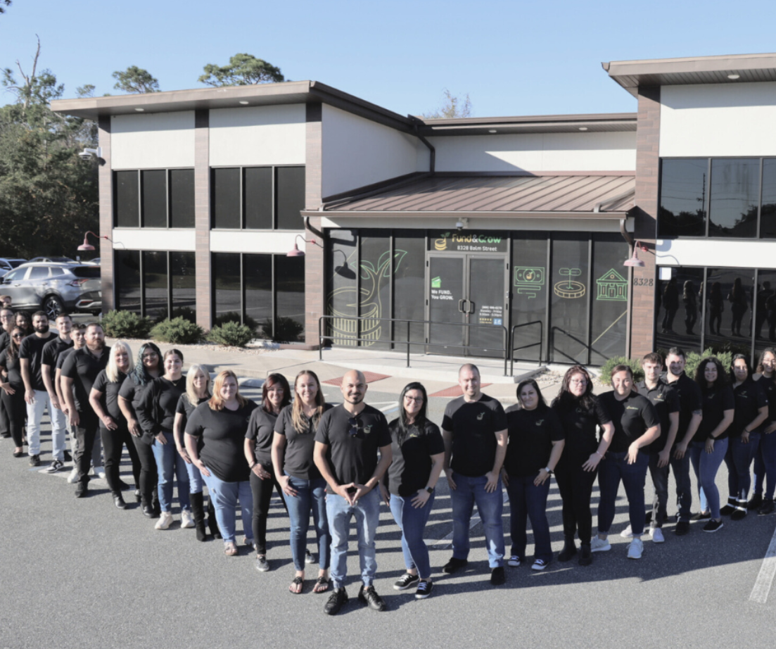 The Fund&Grow team, dressed in matching black company shirts, lines up together outside the Fund&Grow office building.