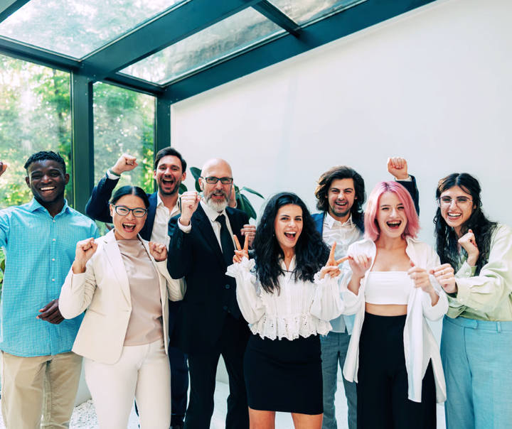 A diverse group of professionals celebrating together in a bright modern space, smiling and raising their fists in excitement.